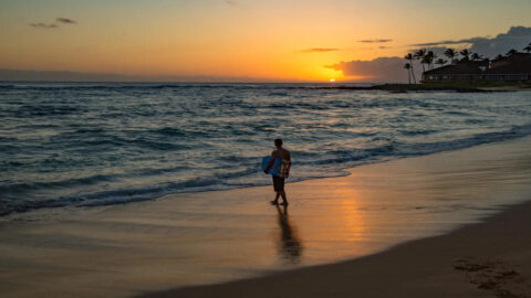 A person with a boogie board walking a Kauai beach at sunset