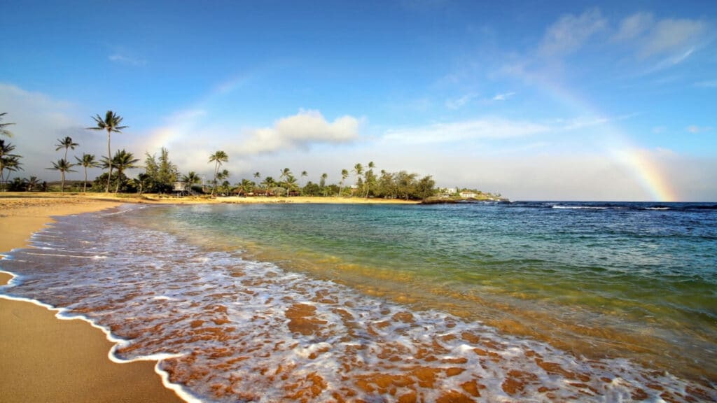 A rainbow over the golden sands and blue waters of Poipu Beach, ranked the #3 beach in America by Dr. Beach