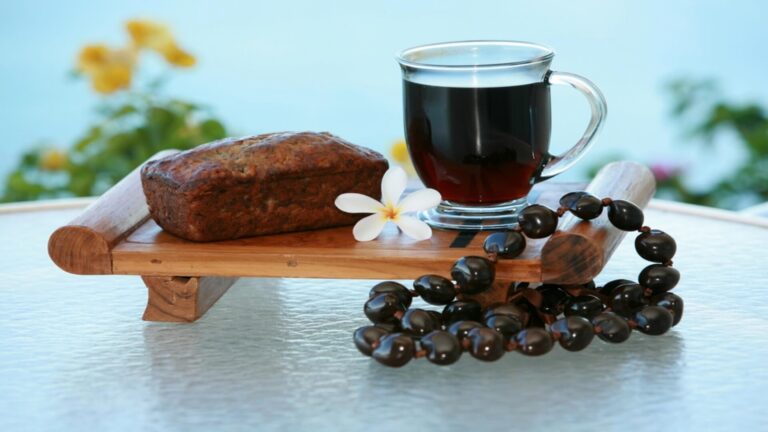 A slice of Hawaiian banana bread on a platter with coffee and a necklace