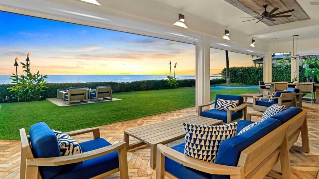 The covered lanai at a luxury vacation home in Kauai, with comfortable seating and views of the ocean and a private pool