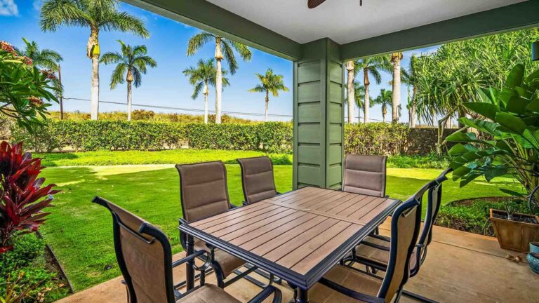 The covered lanai on the ground level of Pili Mai at Poipu #01J with a table and chairs surrounded by lush greenery and palms
