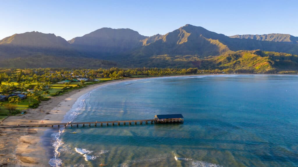 An aerial shot of Hanalei Pier, the bay, and mountains of Kauai